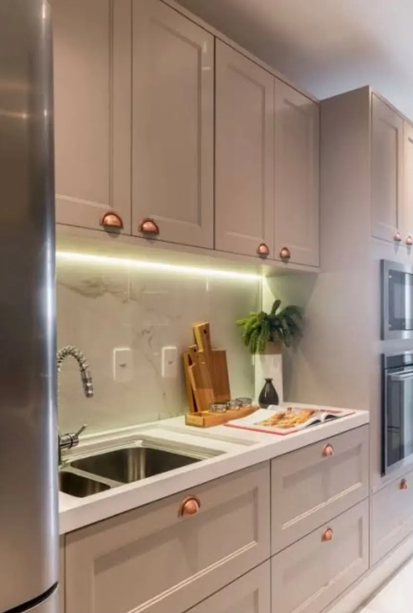Fendi & concha de cobre — Frisado em fendi acetinado, bancada branca, backsplash de mármore e fita de LED sob os armários aéreos.