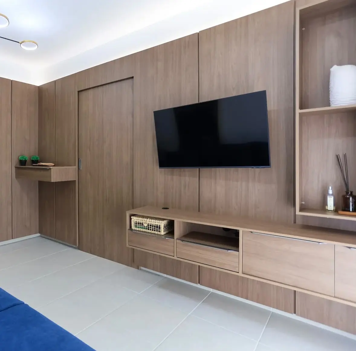 Painel com porta camuflada — Painel amadeirado de parede inteira, rack suspenso com gavetas e a porta do banheiro embutida no mesmo desenho.