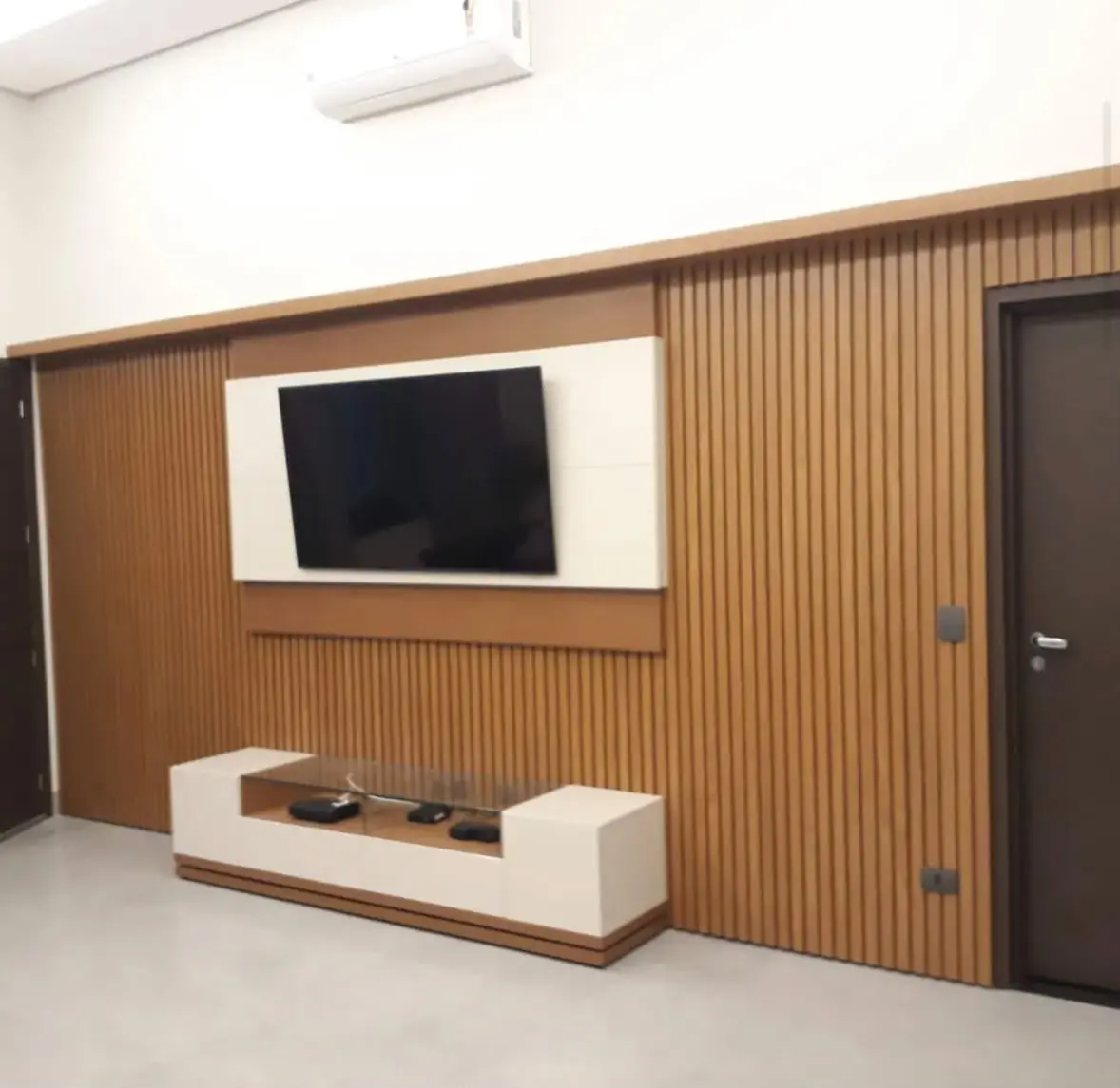 Ripado com porta embutida — Ripado em madeira clara que continua por cima da porta de correr, com rack laqueado branco e base recuada.